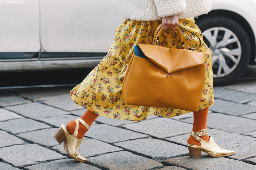 donna con gonna gialla a fiori e cappotto bianco che porta una borsa color senape