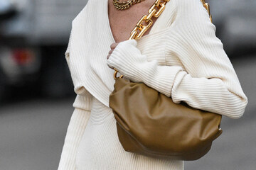 donna in vestito bianco in maglia porta una borsa marrone sulla spalla, la borsa ha una catena d'oro