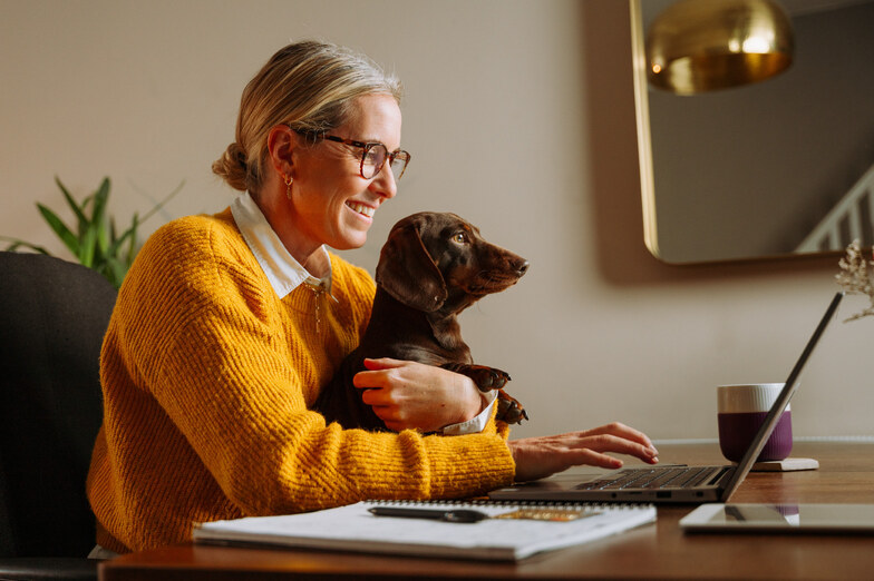donna lavorando a casa, indossa il maglione arancione e tiene il cane
