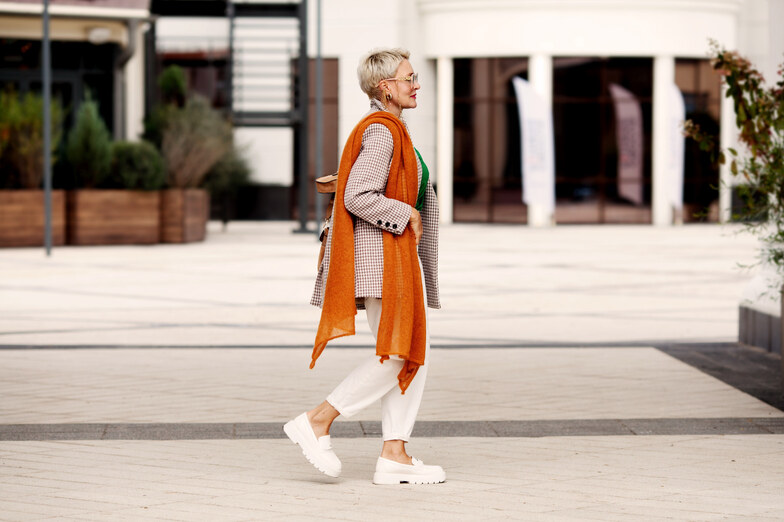donna indosando mocassini bianchi, pantaloni bianchi, blazer e sciarpa arancione