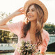 donna sorridente in vestito rosa, cappello di paglia e con dei fiori in mano
